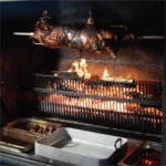 Un cochon entier en train de griller à la broche, sous la surveillance de Gril' Arts et Terroir, professionnel de la grillade au feu de bois, après un méchoui.